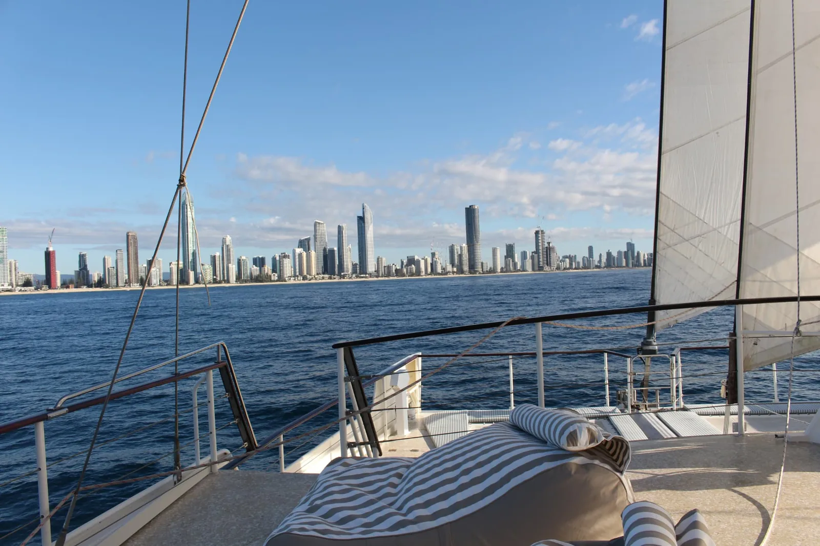 Surfers Paradise skyline seen past the sail from the bow on a Gold Coast sailing voyage aboard VOYŌ