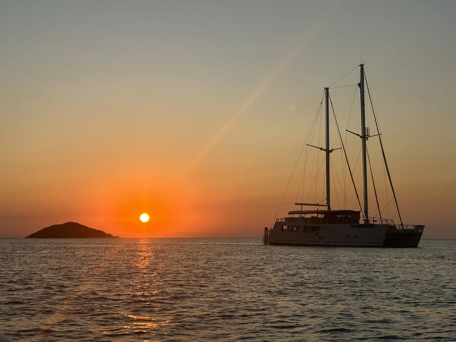 Gold Coast sailing superyacht VOYŌ silhouetted at anchor as the sun sets over the water